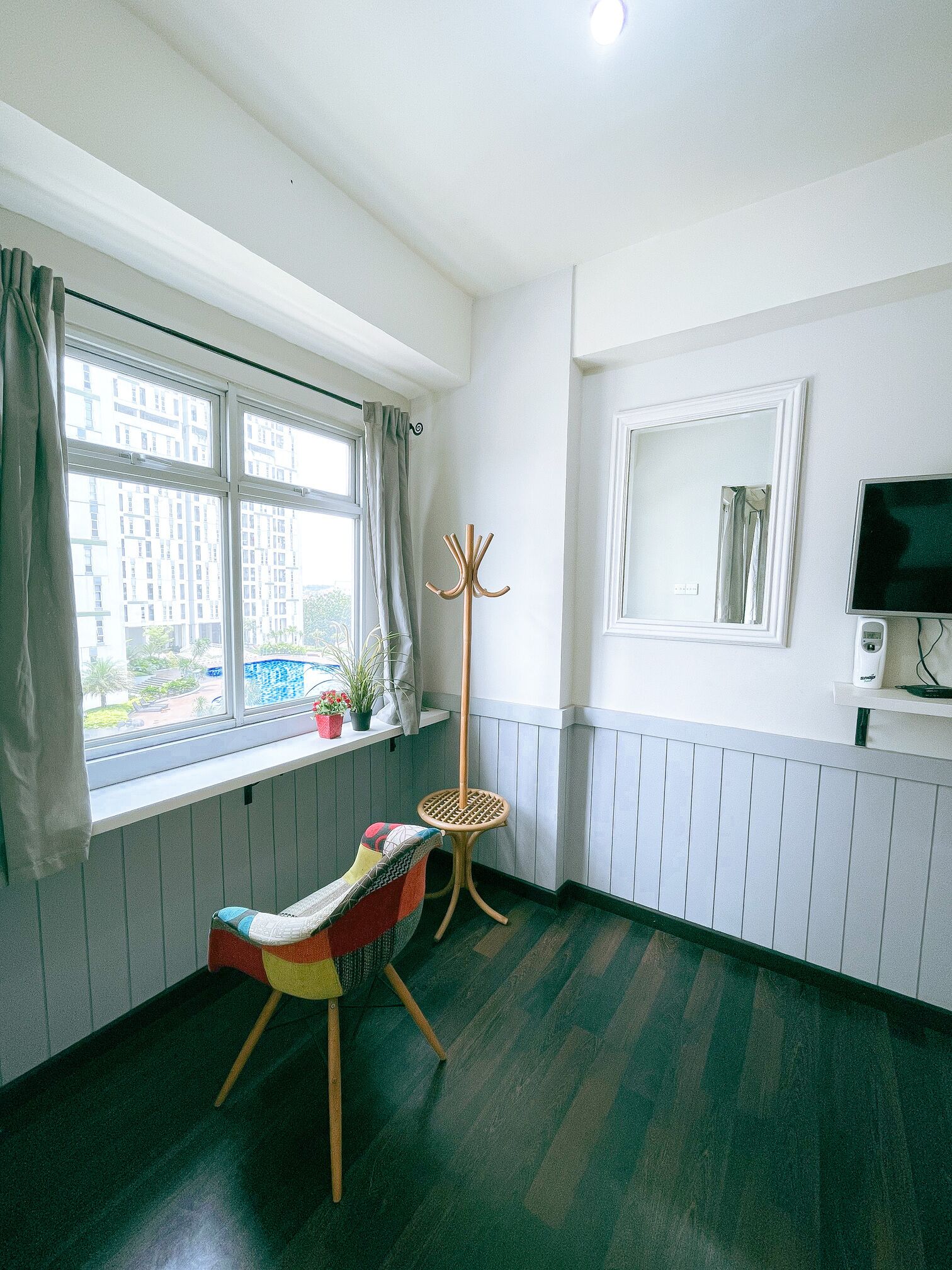 A room with a window, a coat rack, a chair, a small table, and a television.