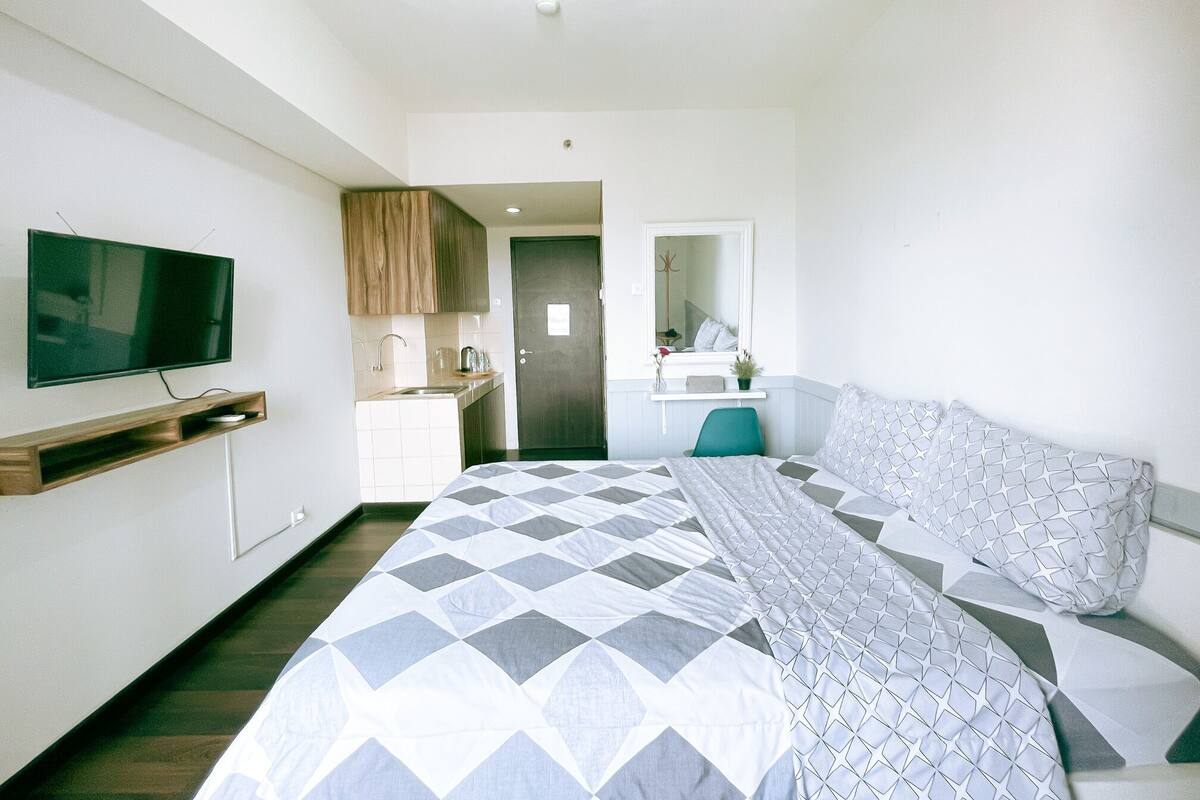 A hotel room with a bed, a TV mounted on the wall, a bathroom with a sink and mirror, and a small window.