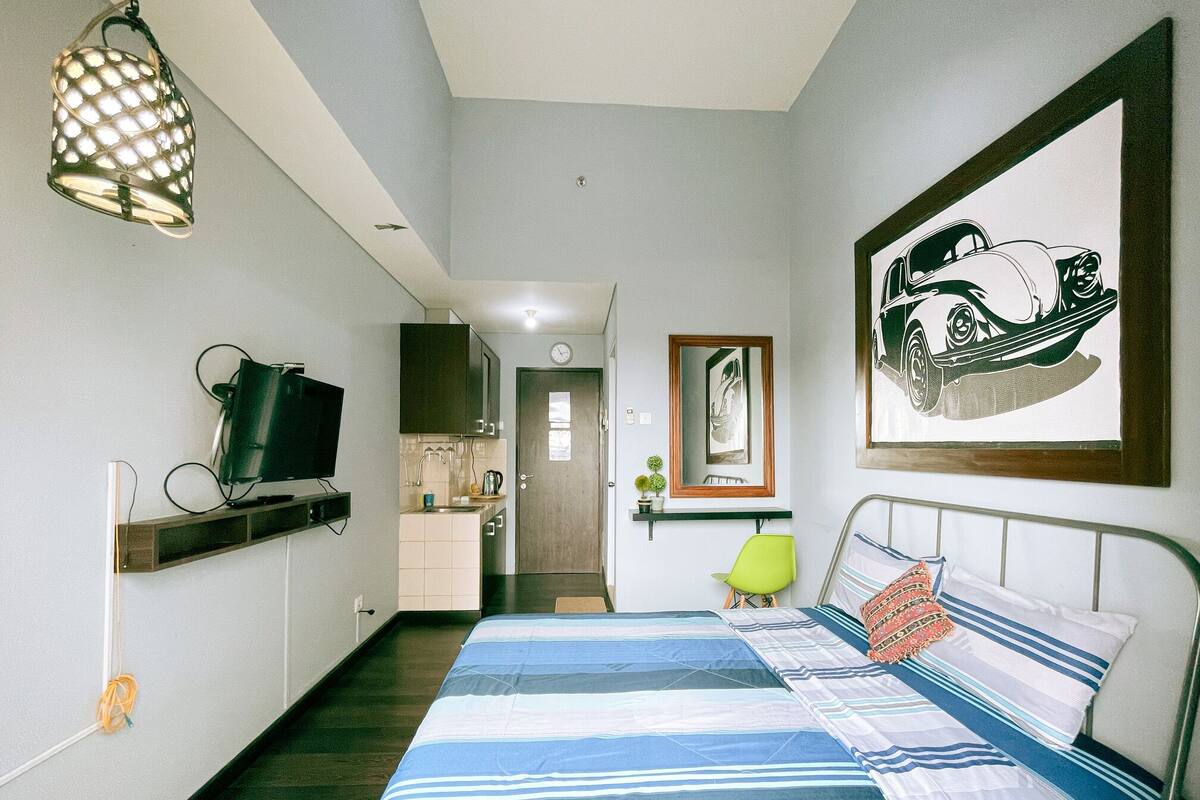 A bedroom with a bed, a TV, a kitchen area, and a bathroom.