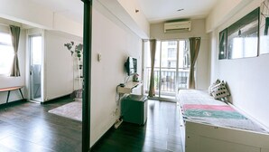 A modern hotel room with a bed, a desk, a chair, a small table, a plant, and a window with curtains. - The Satu Stay Apartement SGV (South Tangerang)