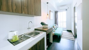 A modern kitchen with a sink, a kettle, and a coffee maker. There is a sofa with cushions in the adjacent living area. - The Satu Stay Apartement SGV (South Tangerang)