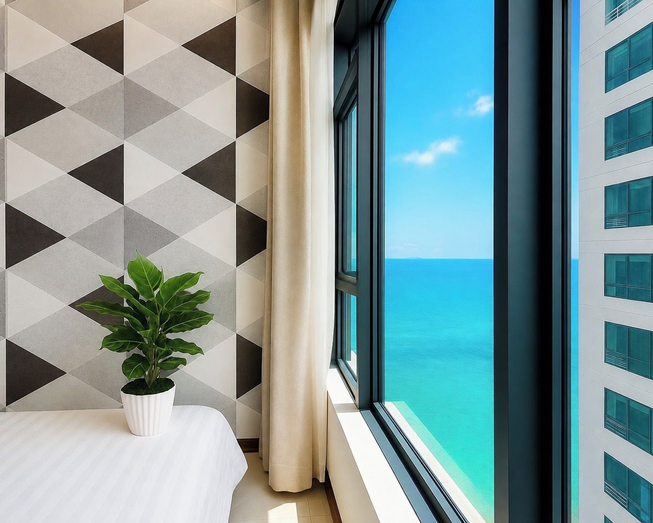 A hotel room with a bed, a potted plant, a window with a view of the sea, and a geometric-patterned wall.