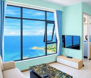 A room with a large window offering a view of the sea, a flat-screen TV, a sofa, and a coffee table. - HQH Sea View Apartment (Bac Nha Trang)