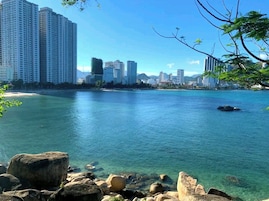 Un paisaje urbano costero con rascacielos, agua azul cristalina y un litoral rocoso.