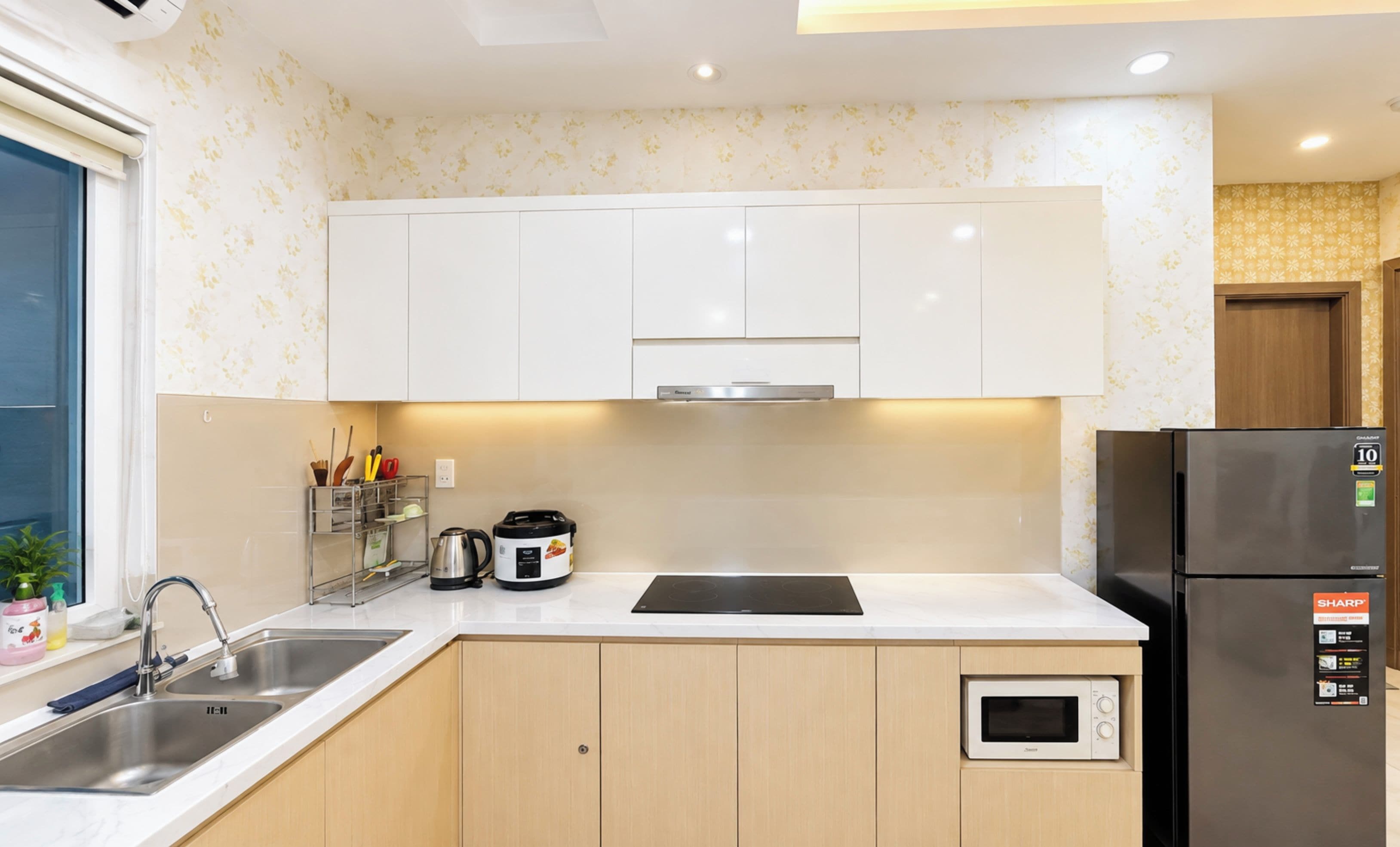A modern kitchen with white cabinets, a stainless steel sink, a built-in microwave, and a refrigerator.
