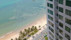Ein Hochhotel mit Blick auf den Strand, mit Balkonen und Geländern, einem Sandstrand und Palmen.