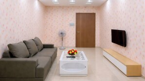 A modern living room with a sofa, coffee table, TV, and recessed ceiling lighting. - HQH Sea View Apartment (Bac Nha Trang)