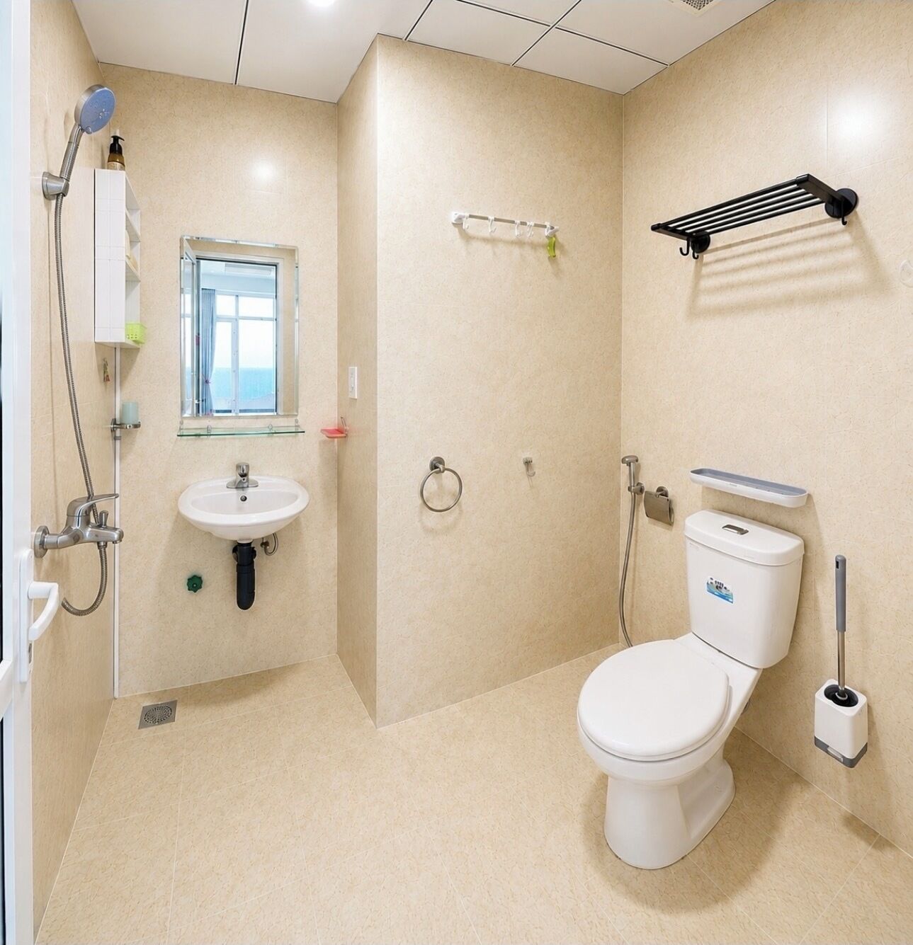 A bathroom with a toilet, sink, shower, towel rack, and a window.