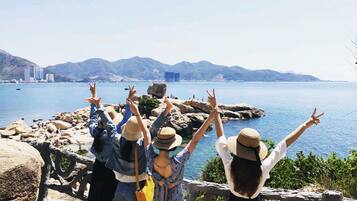 A group of people standing on a rocky seaside with a view of the sea and distant mountains.