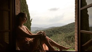 Eine Person sitzt am Fenster mit Blick auf eine hügelige Landschaft.