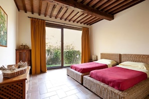 Une chambre avec deux lits, un plafond en bois, une porte-fenêtre coulissante et un banc en osier.