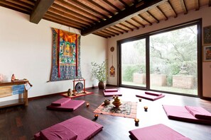 Une salle de méditation avec des poutres en bois, une grande fenêtre et une tapisserie aux couleurs vives.