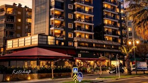 Un hotel de varios pisos con balcones, un restaurante llamado 'Ketchup' en la planta baja y una señal de paso de peatones.
