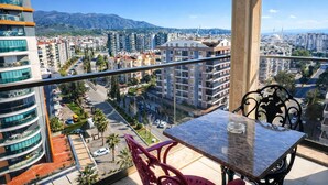 Un balcón con mesa y sillas, con vistas a un paisaje urbano que incluye edificios y montañas.