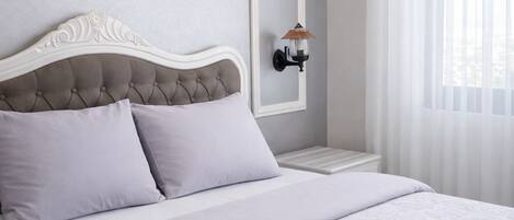 A bedroom with a tufted headboard, a bed with patterned bedding, a nightstand, a wall-mounted lamp, and an air conditioning unit.