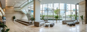 Un vestíbulo amplio con una escalera curva, asientos modernos y grandes ventanales con vistas a la ciudad.