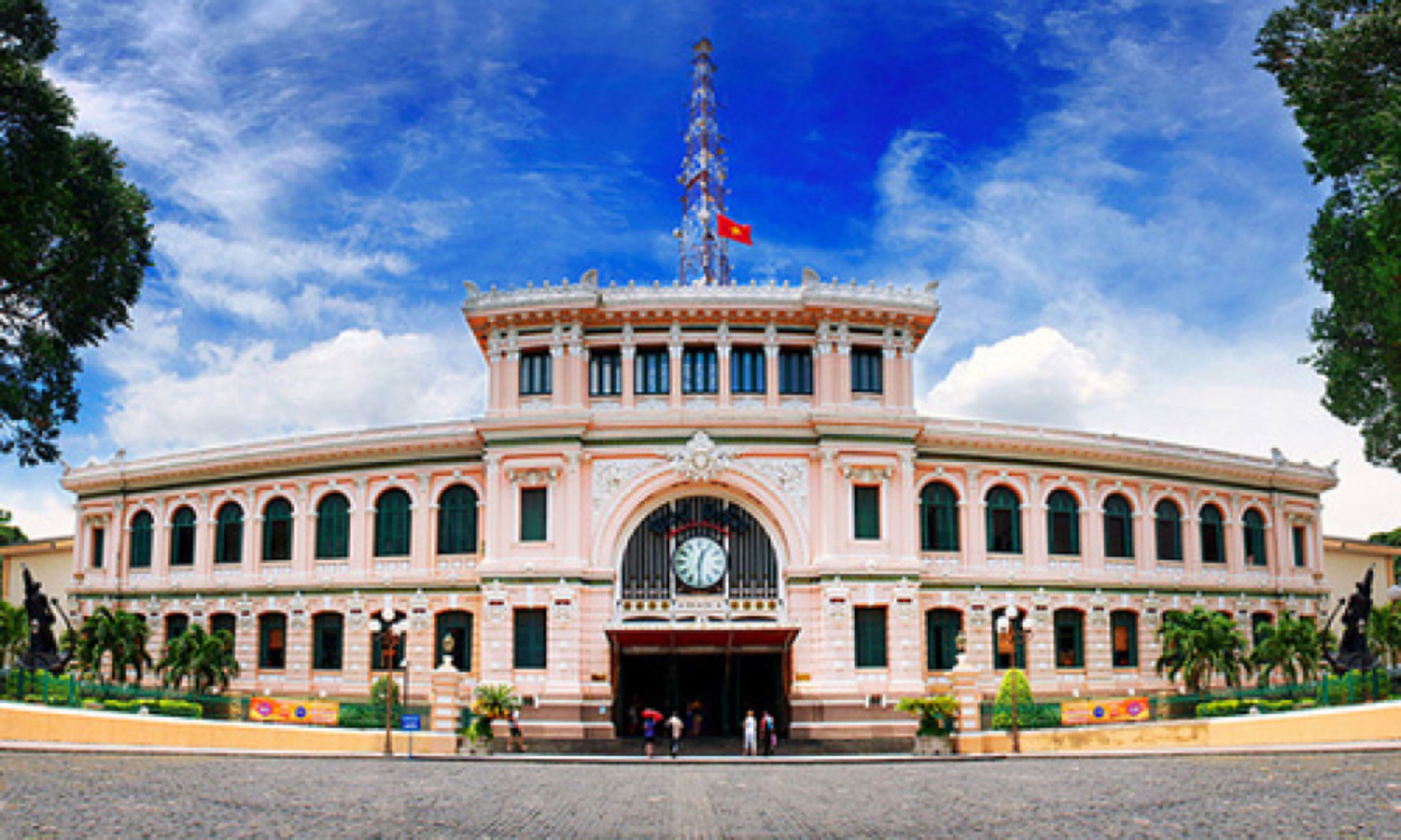 A large, pink, classical-style building with a central clock tower and a flag on top.