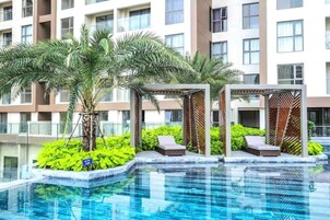 Una piscina rodeada de palmeras, sillas de descanso y un edificio moderno con amplias ventanas.