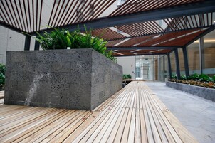 Un espacio exterior moderno con una jardinera de hormigón, suelo de madera y estructura de techo metálica.