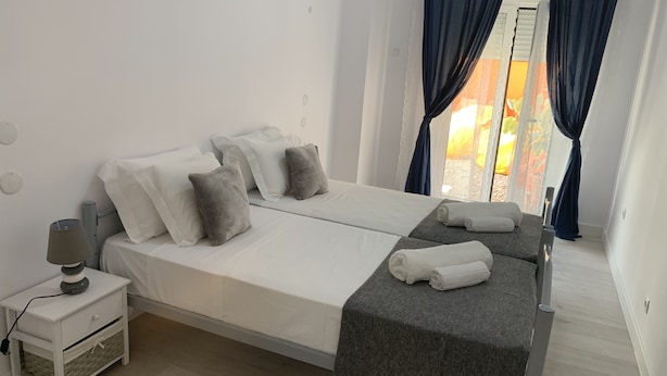 Ein modernes Schlafzimmer mit einem großen Bett, einem Nachttisch mit Lampe und Blick auf einen Garten durch das Fenster.
