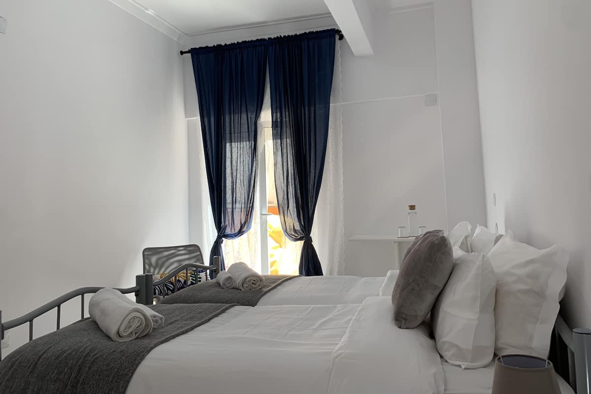 Een moderne hotelkamer met een net opgemaakt bed, een nachtkastje en een raam met blauwe gordijnen.