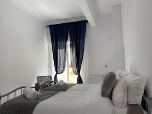 A modern hotel room with a neatly made bed, a bedside table, and a window with blue curtains. - Santo Amaro Guest House (Lisbon)