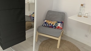 Ein modernes Zimmer mit einem grau gepolsterten Sessel, einem gewebten Teppich und einem weißen Regal mit Glasflaschen.