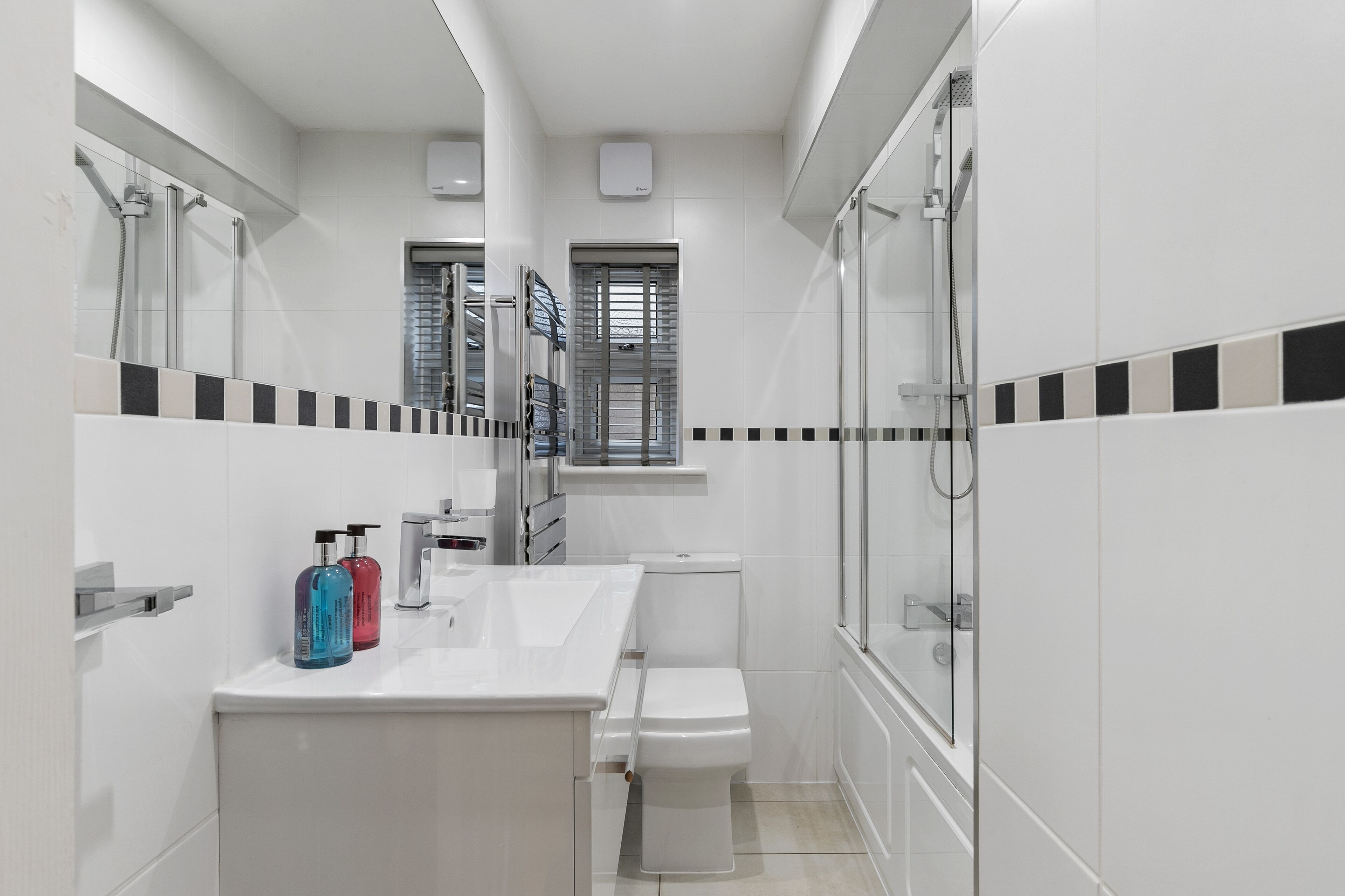 Un baño moderno con lavamanos, inodoro y ducha blancos. Hay dos botellas sobre el encimero del lavamanos.