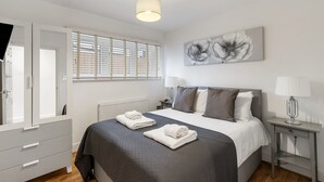 A bedroom with a bed, bedside tables, a window with blinds, a radiator, and a wall-mounted artwork. - St Marks Modern Apartments (Enfield)