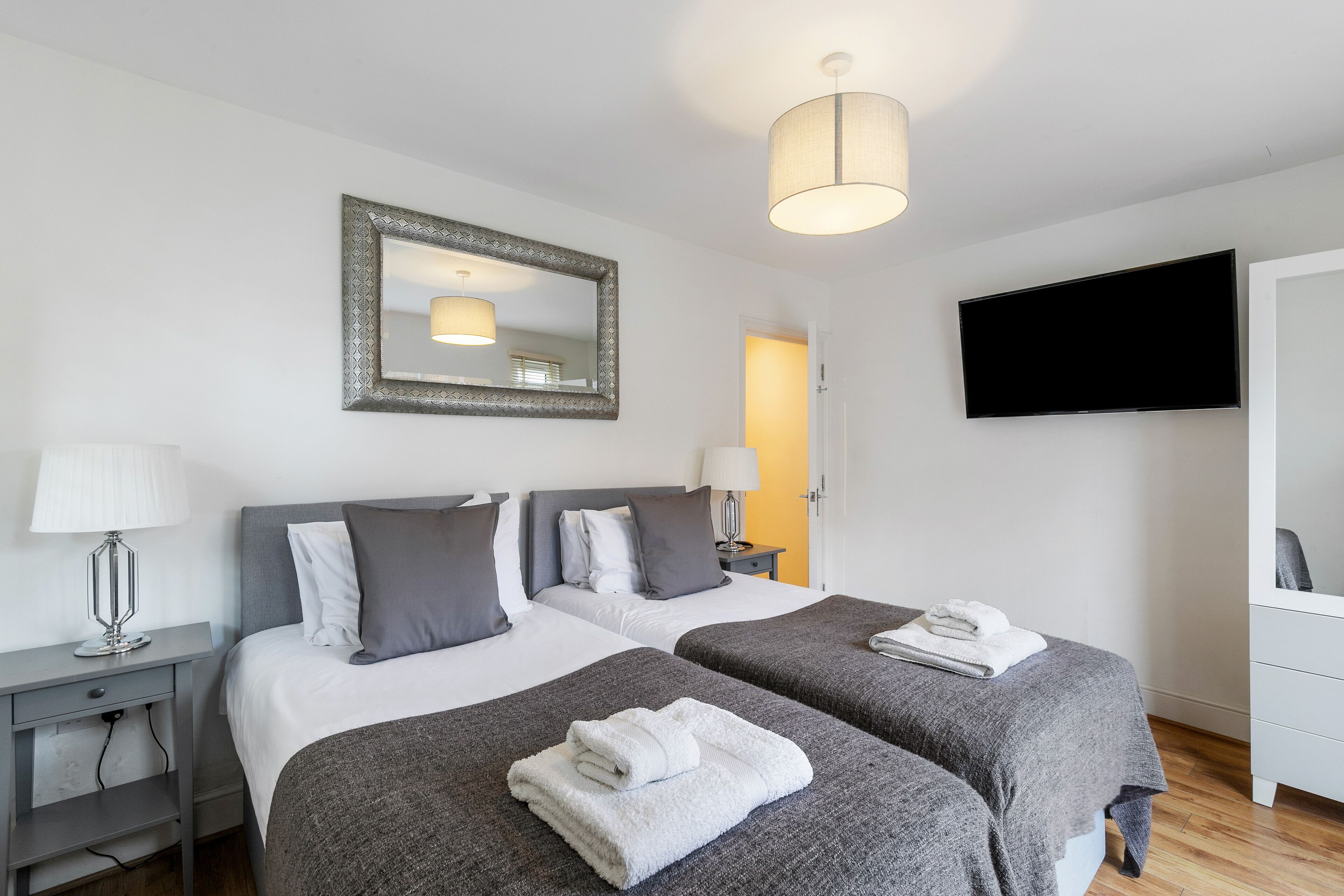 A hotel room with two beds, a TV, a mirror, and a lamp.