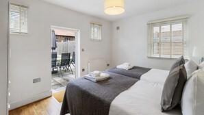 A bedroom with two beds, a ceiling light, and a view of the outside. - St Marks Modern Apartments (Enfield)
