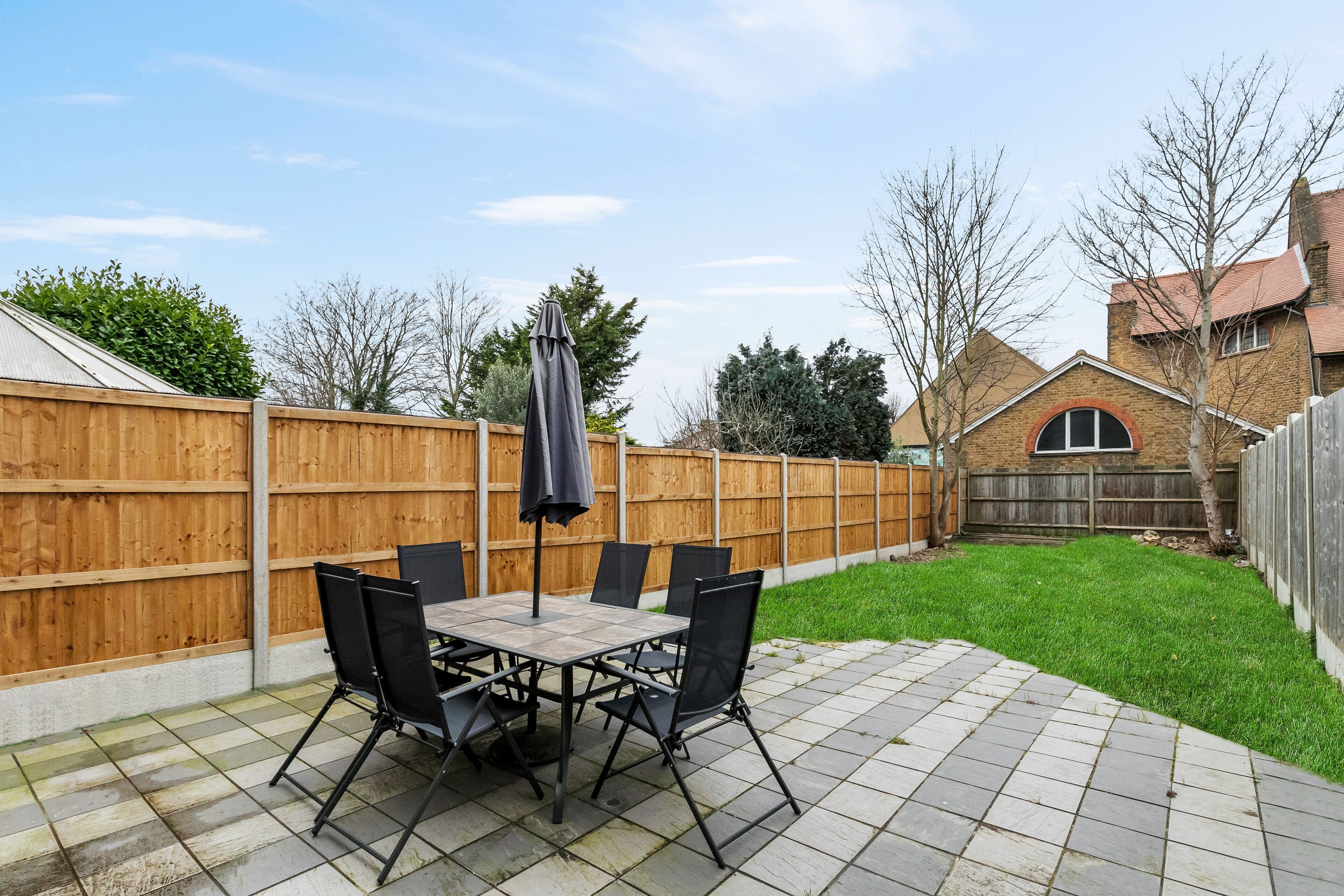 A patio with a table and chairs, a wooden fence, and a house in the background.