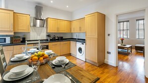 A modern kitchen with wooden cabinets, a stainless steel range hood, and a built-in washing machine. - St Marks Modern Apartments (Enfield)