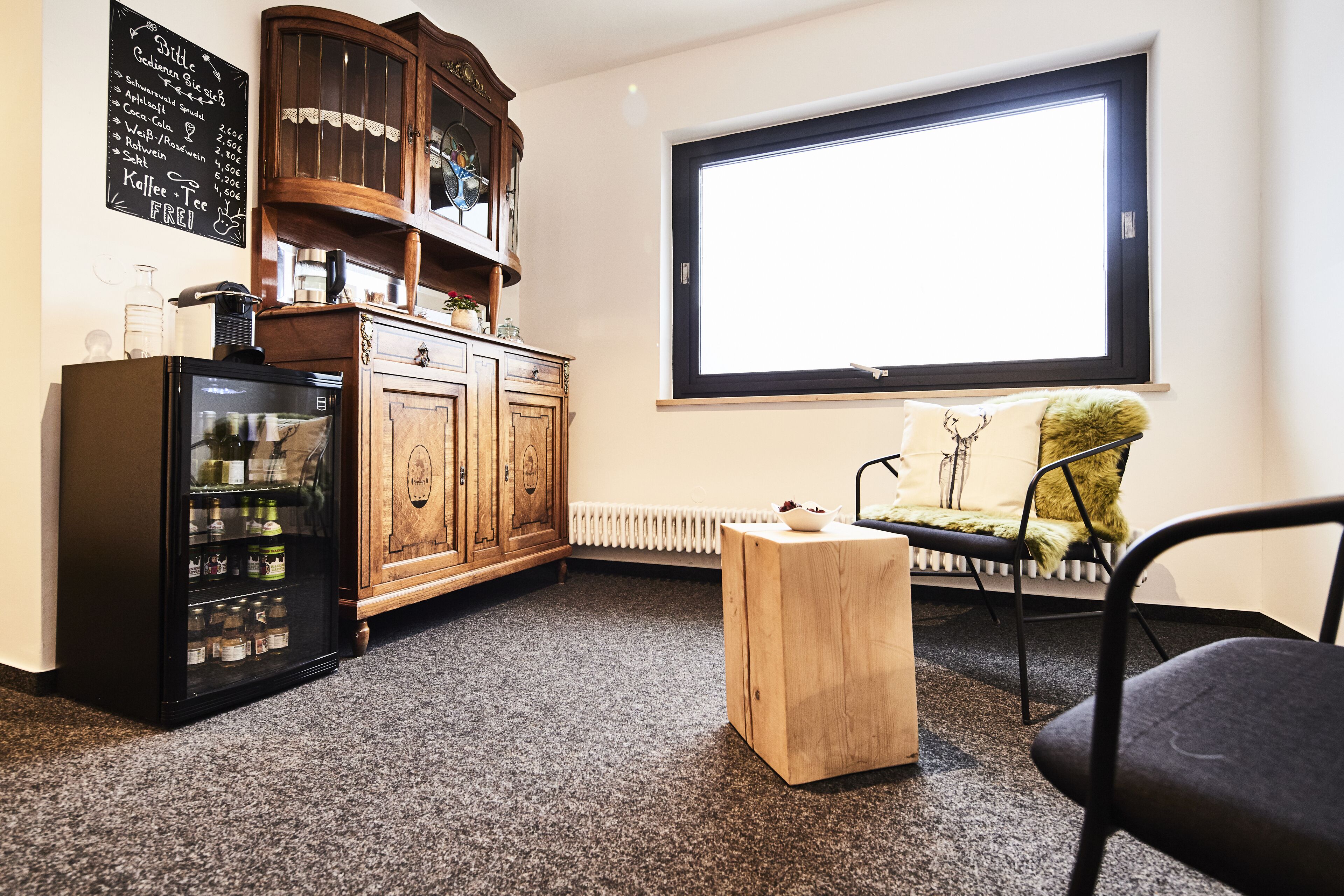 A compact room with a wooden cabinet, a black refrigerator, a wooden side table, and a window with a view.