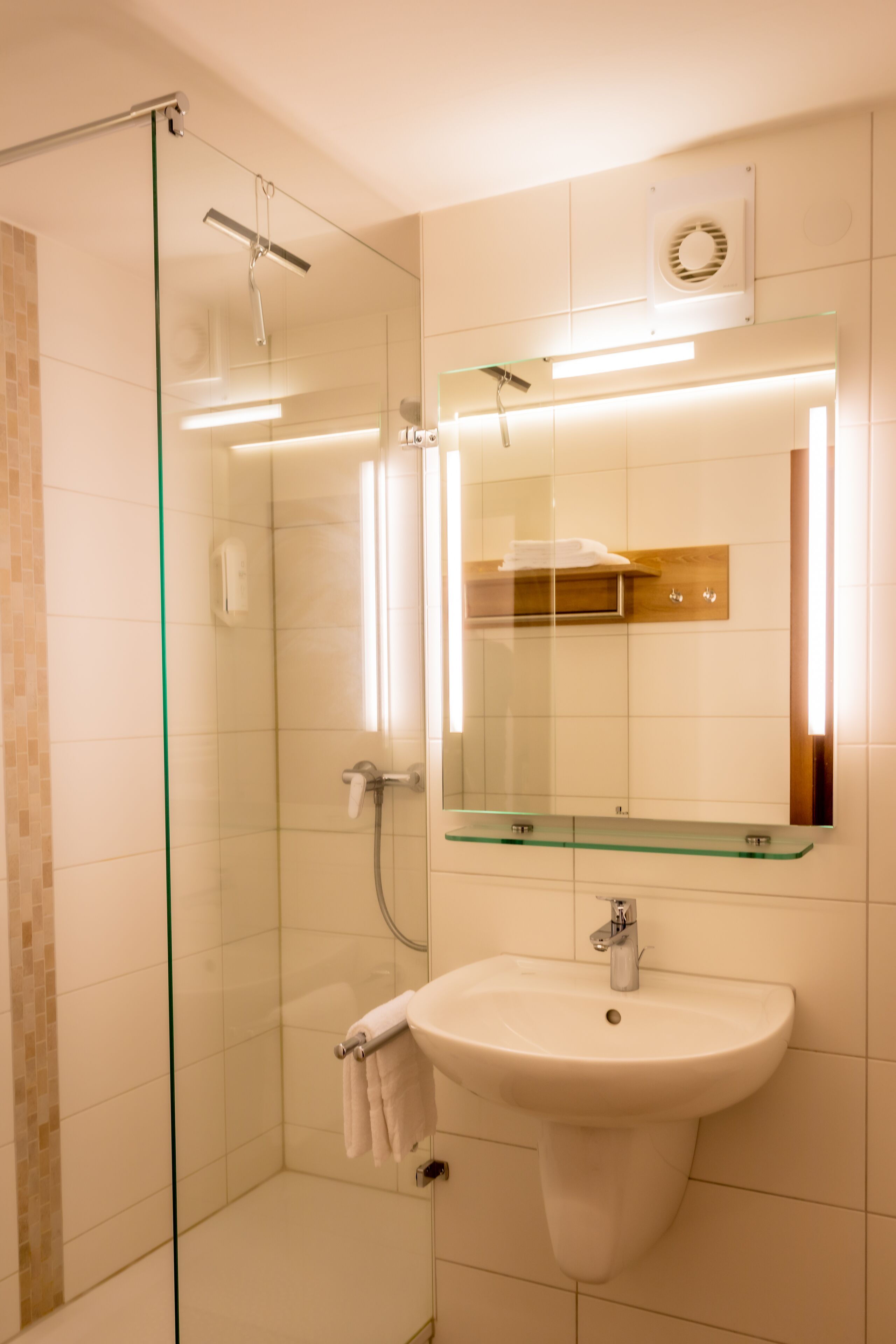 A modern bathroom with a glass shower enclosure, a white sink with a mirror above it, and a towel rack.