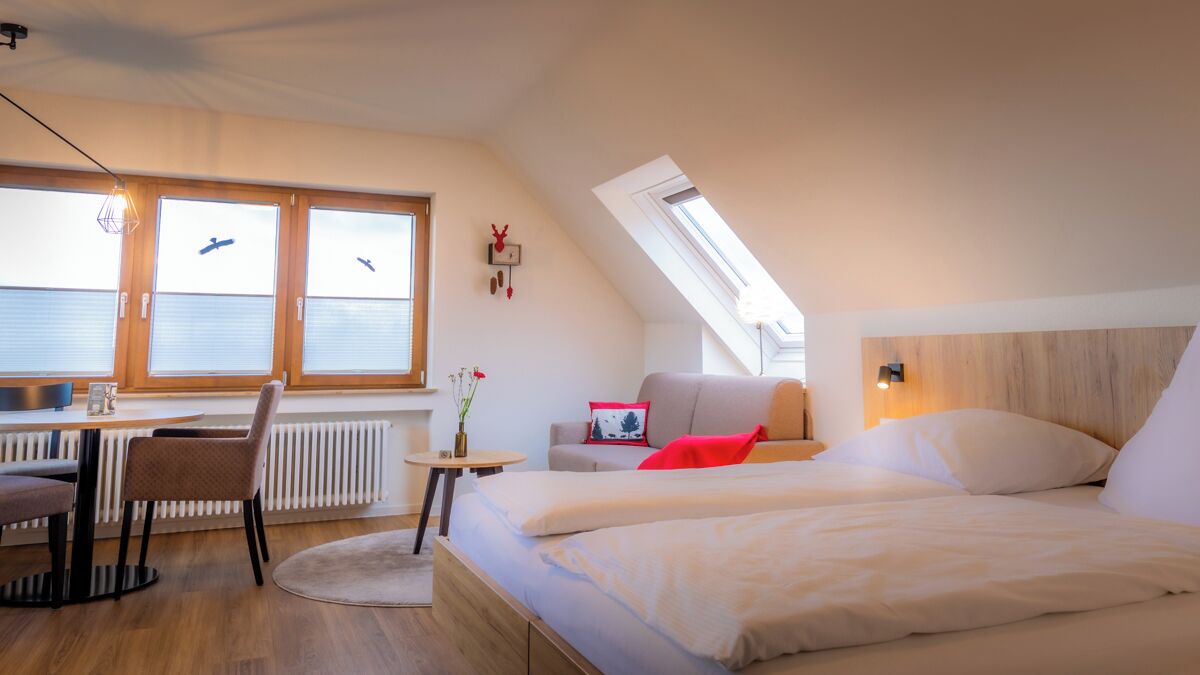 Ein modernes Schlafzimmer mit einem Bett, einem Schreibtisch und einem Stuhl. Ein Fenster mit Jalousien bietet Blick auf den Himmel.