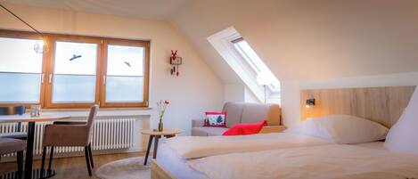 Ein modernes Schlafzimmer mit einem Bett, einem Schreibtisch und einem Stuhl. Ein Fenster mit Jalousien bietet Blick auf den Himmel.
