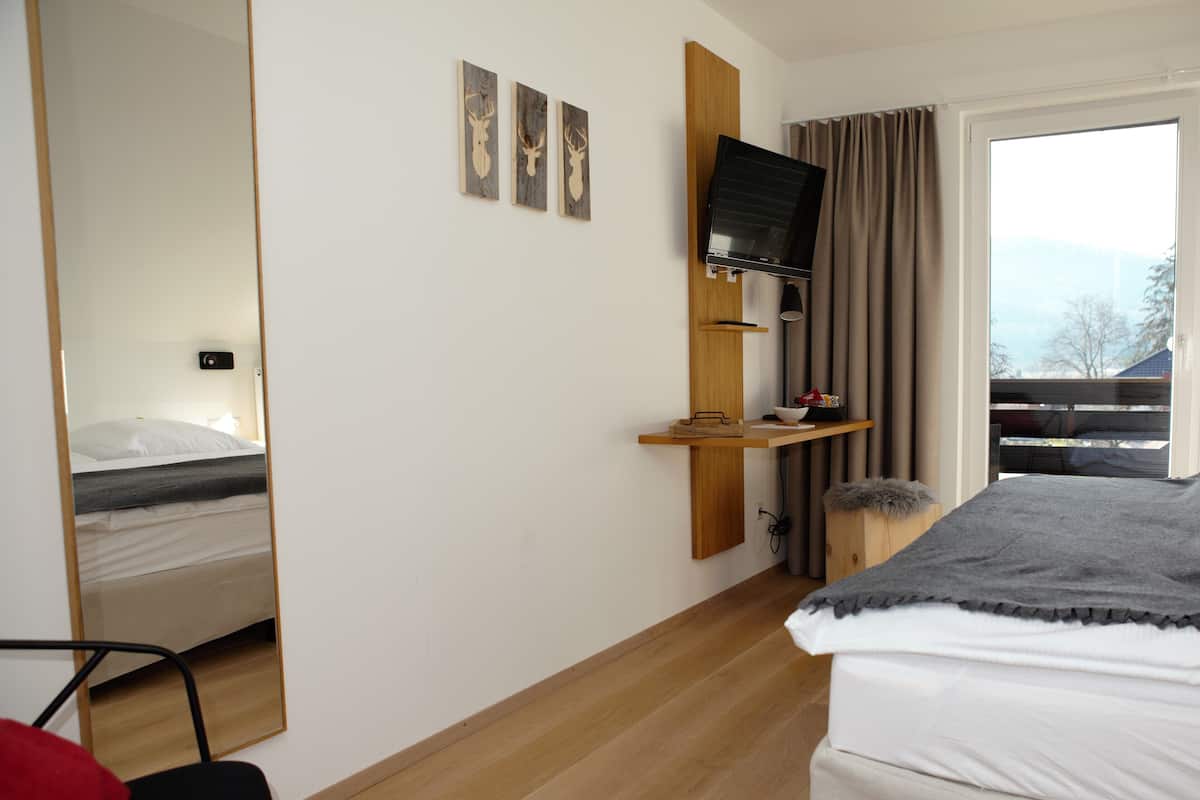 Hotellihuone, jossa on sänky, puuhyllylle asennettu televisio, peili ja ikkuna, jossa on verhot.