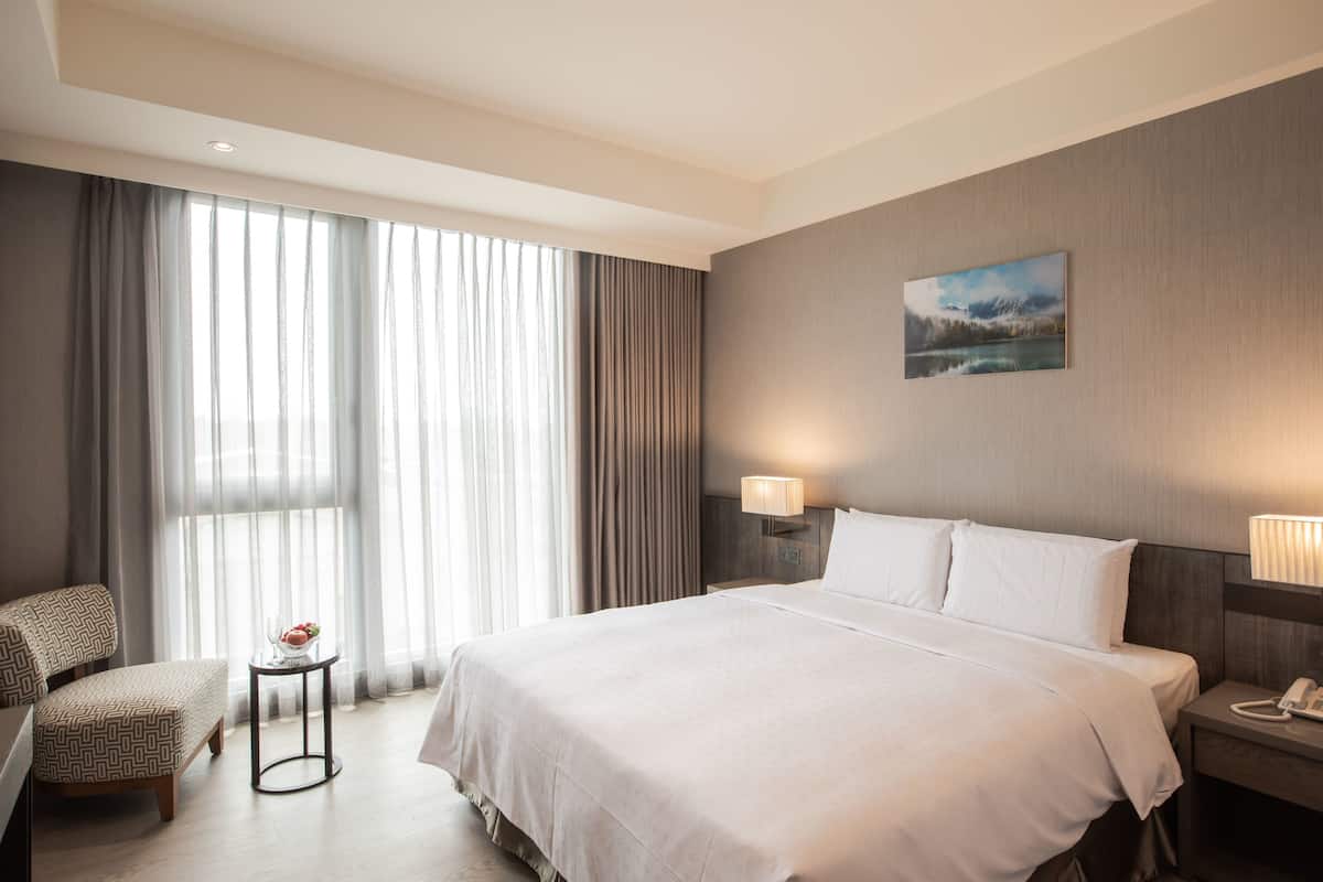Ein Hotelzimmer mit einem großen Bett, einem Sessel, einem kleinen Tisch mit Lampe und einem Bild an der Wand.