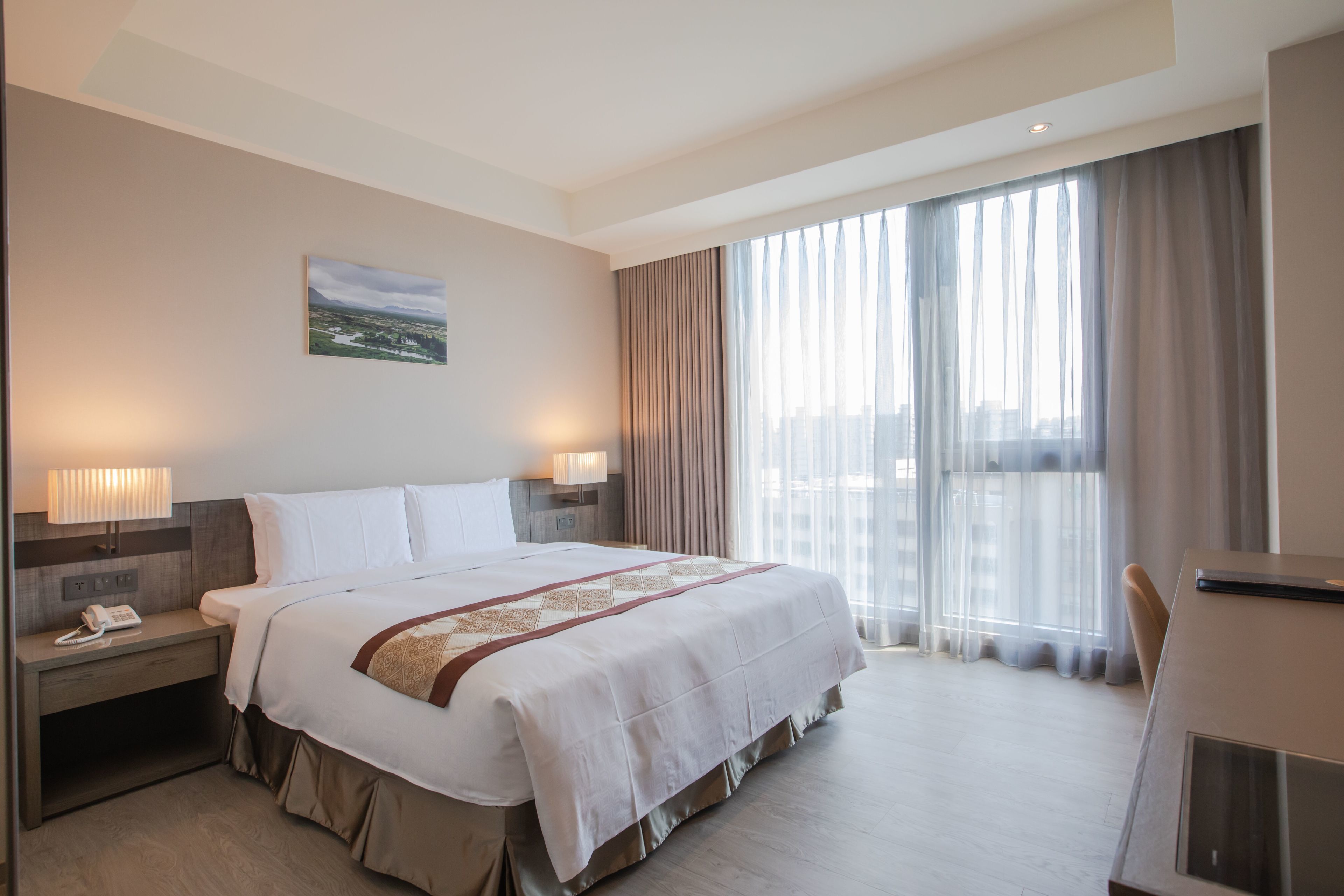 A hotel room with a large bed, bedside lamps, a desk, and a window with curtains.