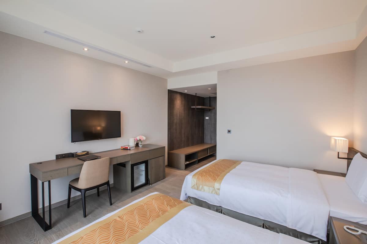 Ein Hotelzimmer mit zwei Betten, einem Schreibtisch, einem Stuhl, einem Fernseher und einer Sitzecke.
