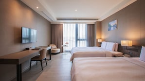 A hotel room with two beds, a desk, a chair, a television, a small table with a vase, and a painting on the wall. - Jin Shi Hu Hotel (Kaohsiung)