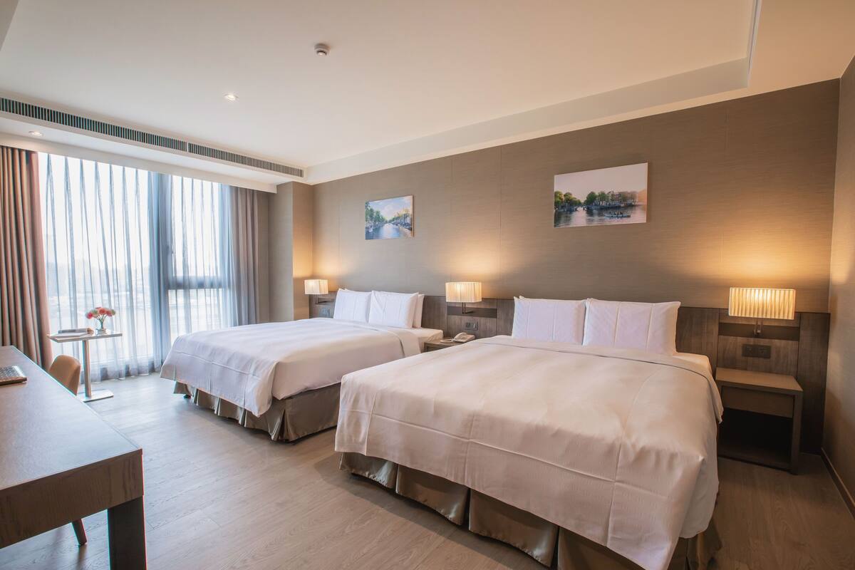 Ein Hotelzimmer mit zwei Betten, einem Schreibtisch und einem kleinen Tisch mit einer Vase.