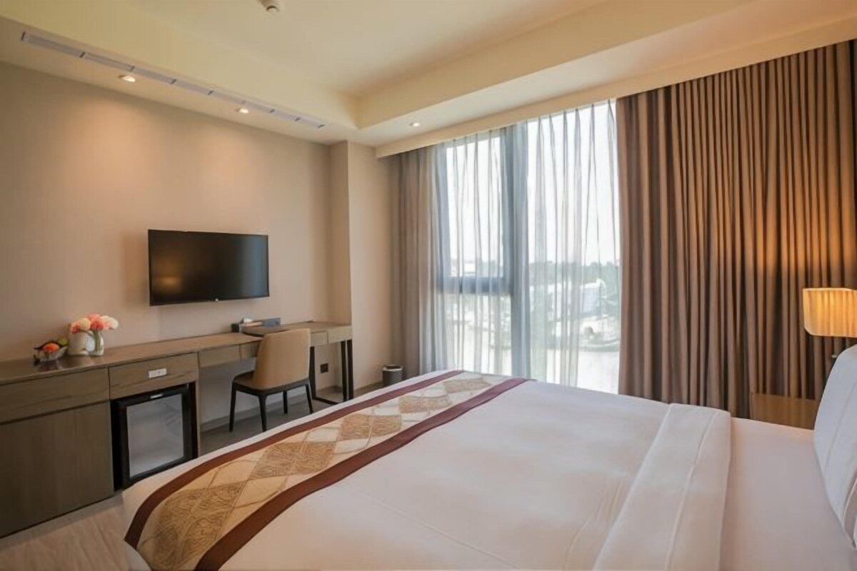 A hotel room with a large bed, a desk, a television, and a view of the outdoors.