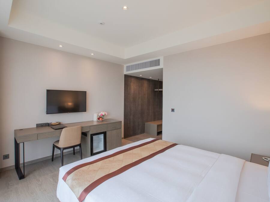 A hotel room with a bed, a desk, a chair, a television, and a wardrobe.
