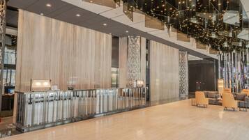 A spacious lobby with a modern design, featuring a reception desk, seating area, and a staircase with glass railings.