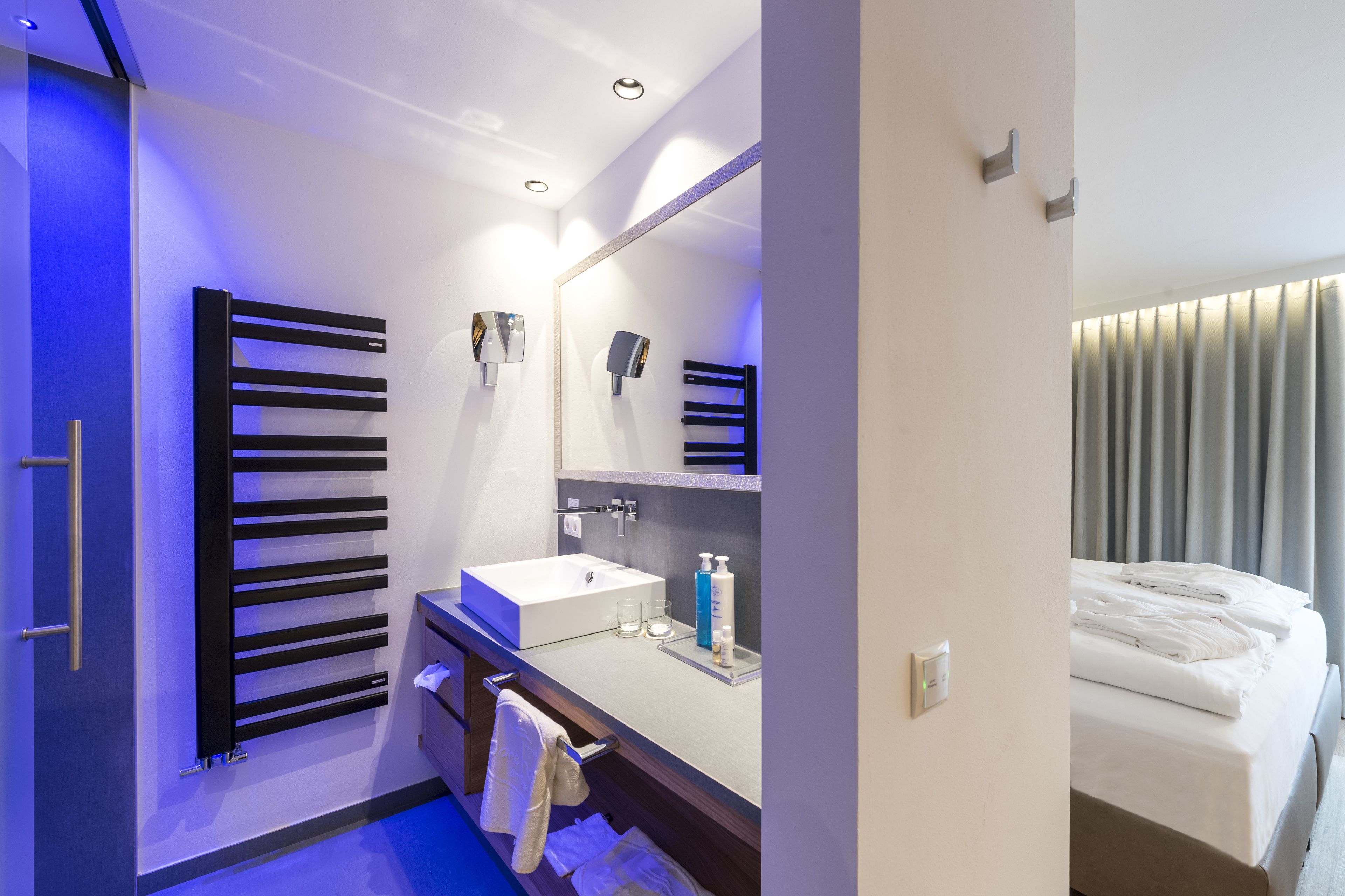 A modern hotel bathroom with a large mirror, a white sink, and a towel rack.