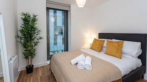 Een moderne hotelkamer met een groot bed, een plant in pot en uitzicht op de stad door een glazen deur.