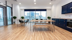 Een moderne keuken met houten vloeren, een eethoek met tafels en stoelen, en een uitzicht op de stad door grote ramen.