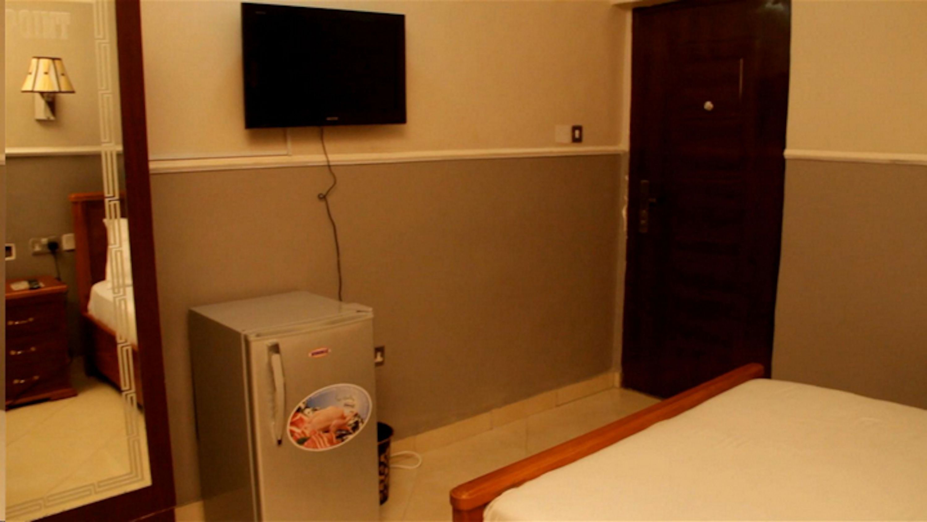 A small room with a bed, a television mounted on the wall, a small safe, and a door.
